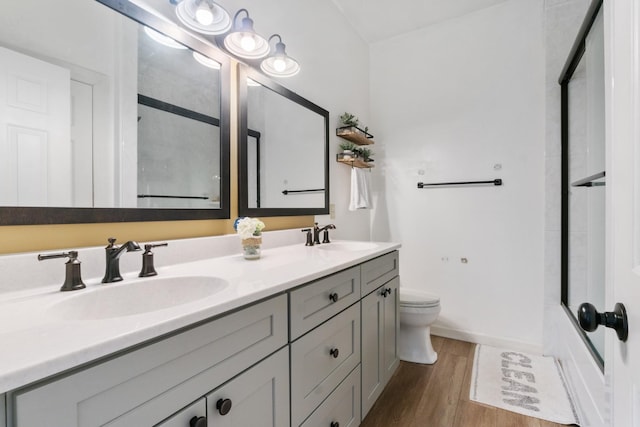 full bathroom with vanity, wood-type flooring, combined bath / shower with glass door, and toilet