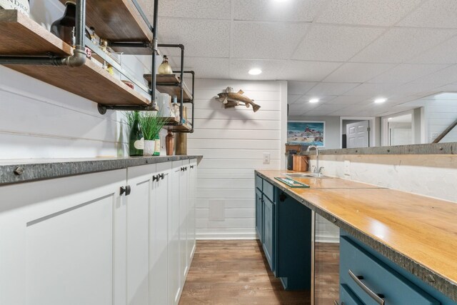 kitchen with a drop ceiling, wine cooler, blue cabinets, butcher block countertops, and light wood-type flooring