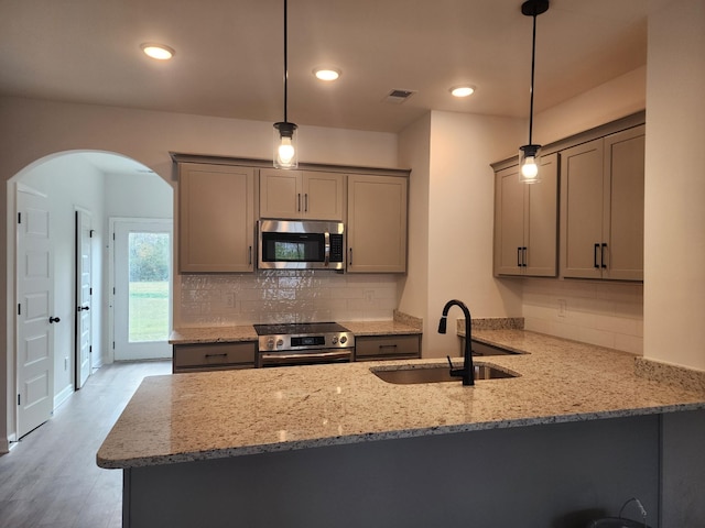 kitchen featuring sink, light hardwood / wood-style flooring, kitchen peninsula, pendant lighting, and appliances with stainless steel finishes