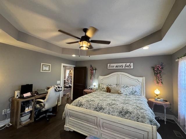 bedroom with ceiling fan, dark wood-type flooring, and a tray ceiling