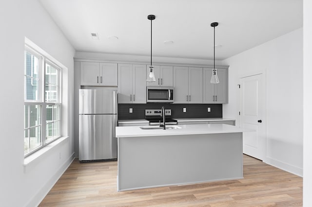 kitchen with decorative light fixtures, a kitchen island with sink, stainless steel appliances, and a wealth of natural light