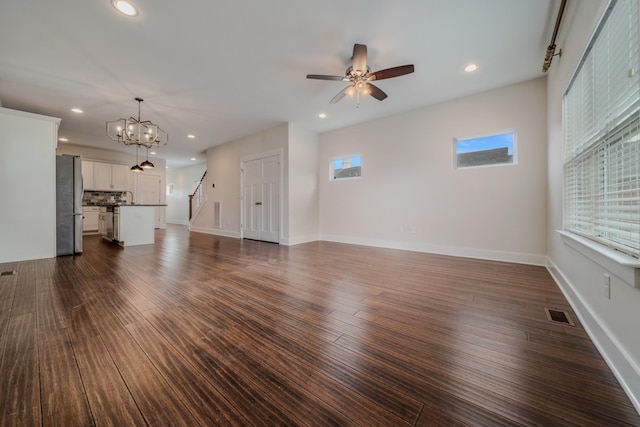 unfurnished living room featuring dark hardwood / wood-style flooring and ceiling fan with notable chandelier