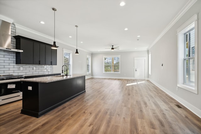 kitchen featuring gas range, wall chimney exhaust hood, hanging light fixtures, tasteful backsplash, and an island with sink