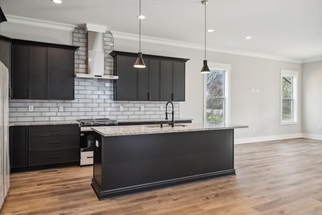 kitchen with a center island with sink, wall chimney range hood, sink, hanging light fixtures, and range with gas stovetop