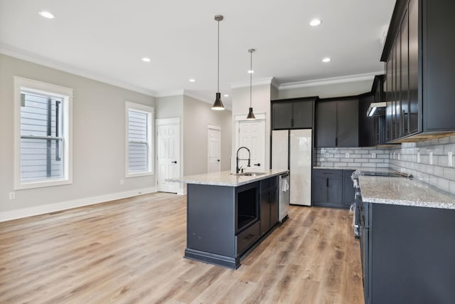 kitchen featuring sink, tasteful backsplash, light hardwood / wood-style floors, decorative light fixtures, and a center island with sink