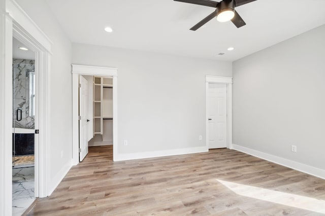 unfurnished bedroom with a spacious closet, a closet, ceiling fan, and light wood-type flooring