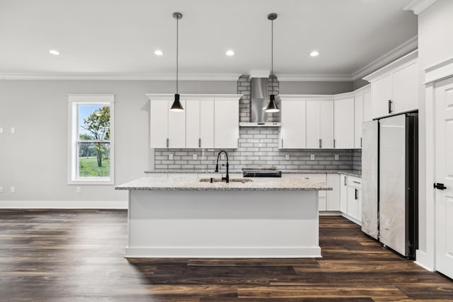 kitchen with white cabinets, stainless steel fridge, wall chimney range hood, and hanging light fixtures