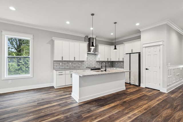 kitchen with refrigerator, wall chimney exhaust hood, dark wood-type flooring, white cabinetry, and an island with sink