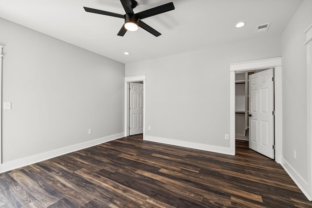 unfurnished bedroom featuring a walk in closet, dark hardwood / wood-style flooring, a closet, and ceiling fan