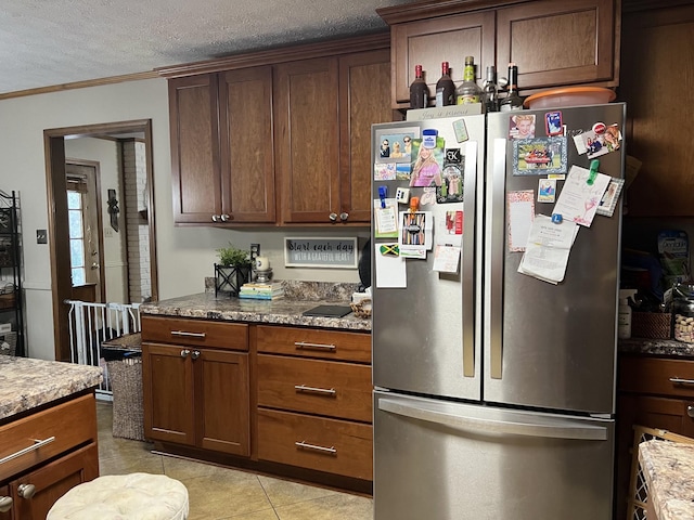 kitchen featuring light stone countertops, light tile patterned floors, a textured ceiling, and stainless steel refrigerator