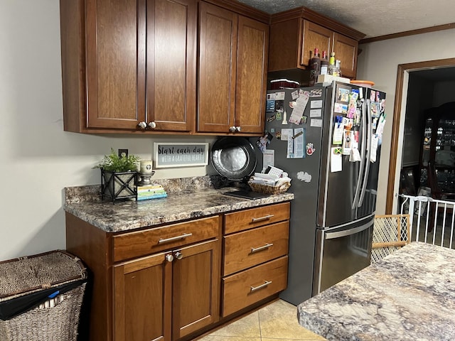 kitchen featuring stainless steel fridge, a textured ceiling, crown molding, light tile patterned floors, and dark stone countertops