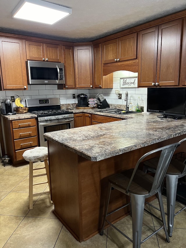 kitchen featuring a kitchen bar, kitchen peninsula, backsplash, and appliances with stainless steel finishes