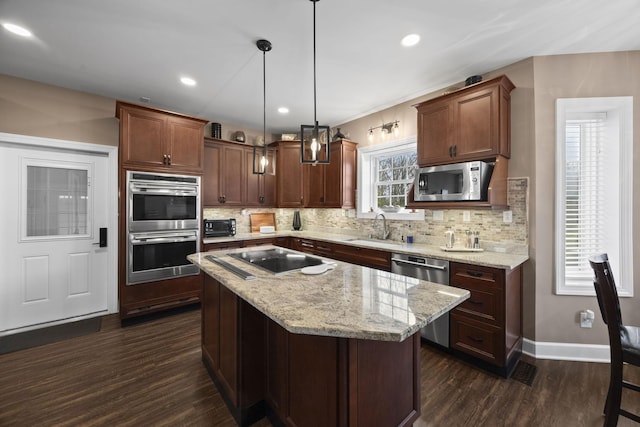 kitchen featuring dark wood-type flooring, sink, hanging light fixtures, a kitchen island, and stainless steel appliances