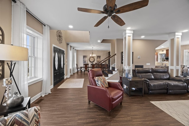 living room featuring ceiling fan with notable chandelier, ornate columns, and dark wood-type flooring