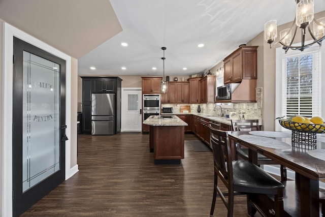 kitchen featuring light stone countertops, a center island, stainless steel appliances, tasteful backsplash, and decorative light fixtures