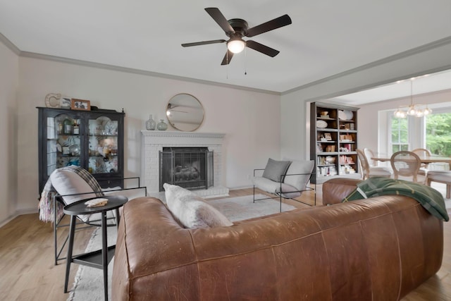 living room with ceiling fan with notable chandelier, crown molding, a fireplace, and light hardwood / wood-style flooring