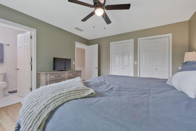 bedroom featuring two closets, ensuite bathroom, light hardwood / wood-style flooring, and ceiling fan