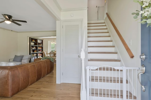 stairs with crown molding, ceiling fan with notable chandelier, and hardwood / wood-style flooring