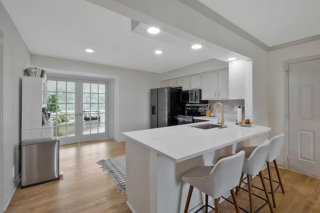 kitchen featuring white cabinetry, sink, tasteful backsplash, appliances with stainless steel finishes, and light wood-type flooring