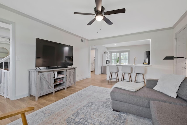 living room featuring ceiling fan, ornamental molding, sink, and light hardwood / wood-style flooring