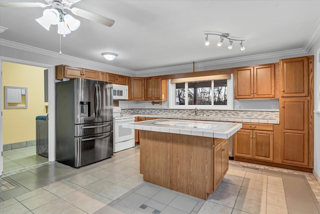 kitchen with a center island, white appliances, backsplash, light tile patterned floors, and tile counters