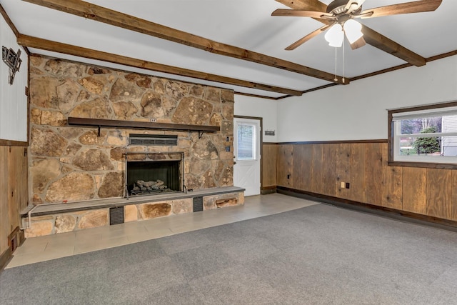 unfurnished living room with wooden walls, ceiling fan, a fireplace, beamed ceiling, and carpet floors