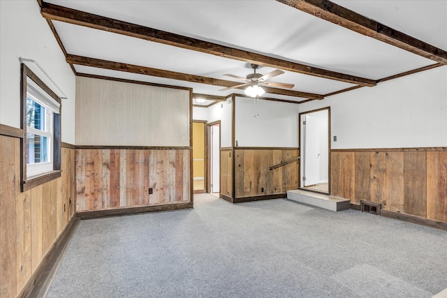 carpeted empty room featuring beamed ceiling, ceiling fan, and wooden walls