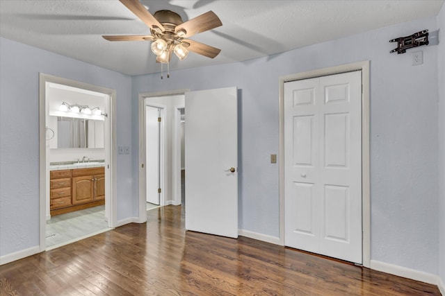 unfurnished bedroom featuring connected bathroom, ceiling fan, sink, dark hardwood / wood-style flooring, and a textured ceiling