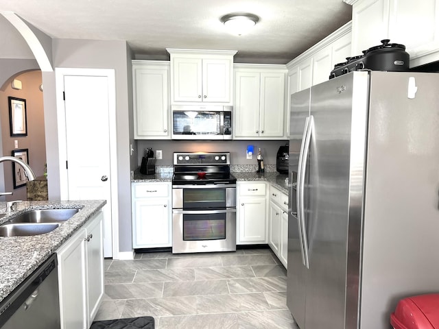 kitchen featuring white cabinets, appliances with stainless steel finishes, light stone counters, and sink