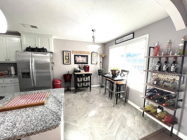 kitchen with decorative light fixtures, dark stone countertops, white cabinetry, and stainless steel refrigerator with ice dispenser