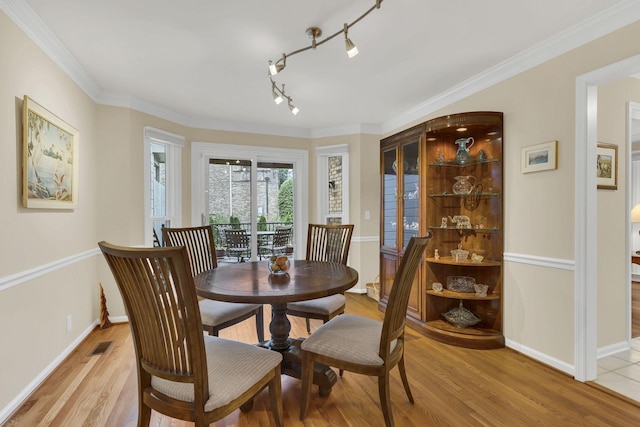 dining space featuring light wood-type flooring, track lighting, and crown molding