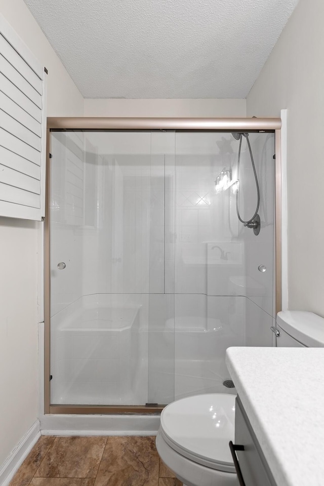 bathroom with a textured ceiling, toilet, and a shower with shower door