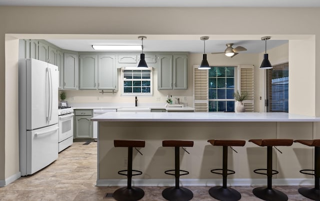 kitchen with kitchen peninsula, white appliances, sink, hanging light fixtures, and a breakfast bar area