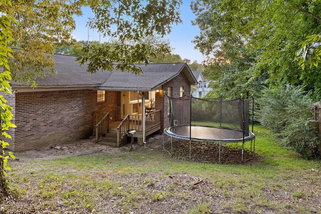 rear view of house featuring a trampoline, a lawn, and a wooden deck