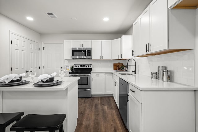 kitchen with a kitchen breakfast bar, dark hardwood / wood-style flooring, stainless steel appliances, sink, and white cabinetry