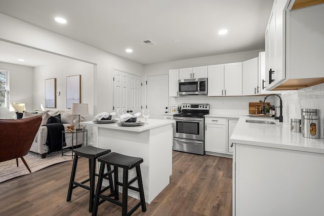 kitchen with dark wood-type flooring, a kitchen breakfast bar, sink, white cabinetry, and stainless steel appliances