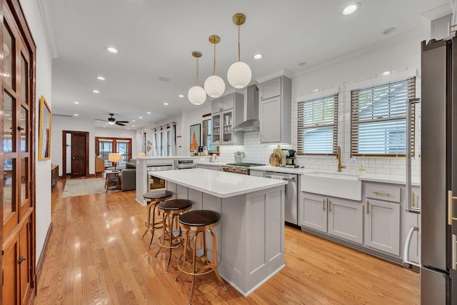 kitchen with sink, wall chimney range hood, light hardwood / wood-style floors, decorative light fixtures, and appliances with stainless steel finishes