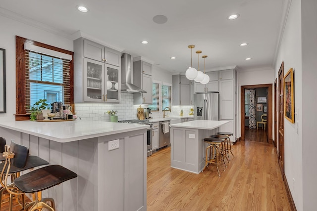 kitchen with wall chimney exhaust hood, pendant lighting, a breakfast bar area, appliances with stainless steel finishes, and light wood-type flooring