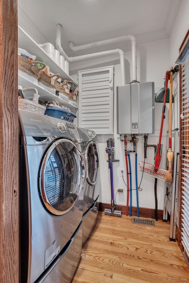 clothes washing area with washing machine and clothes dryer, light hardwood / wood-style flooring, ornamental molding, and water heater