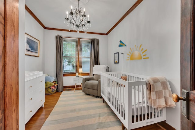 bedroom featuring a notable chandelier, light hardwood / wood-style floors, a crib, and ornamental molding