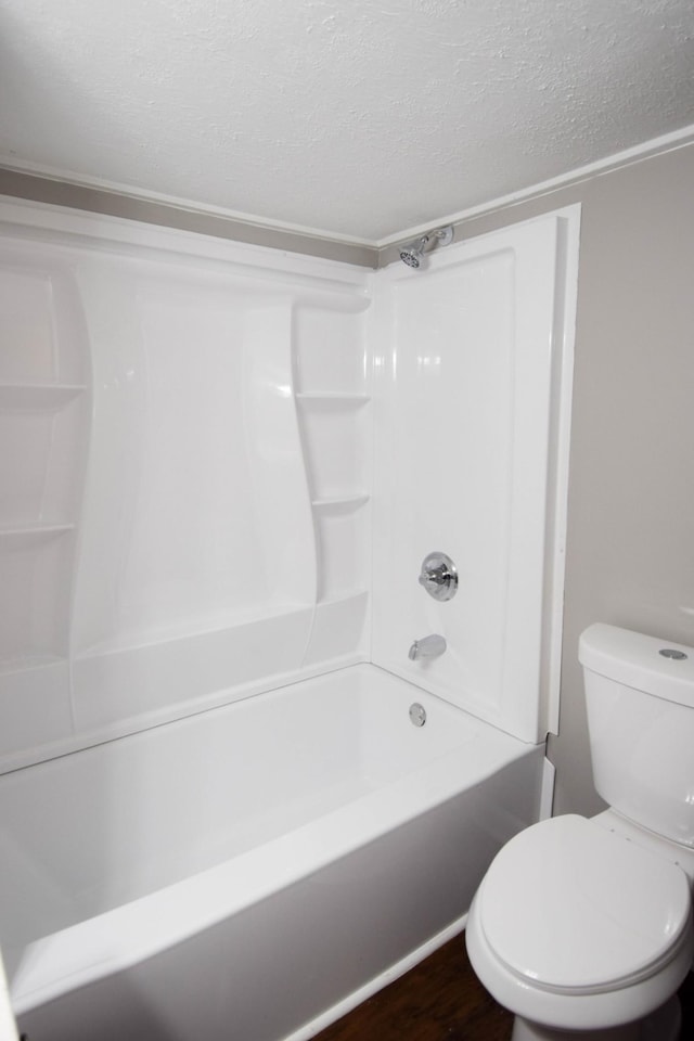 bathroom with toilet, a textured ceiling, and bathing tub / shower combination