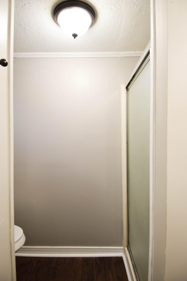 bathroom with wood-type flooring, toilet, ornamental molding, a textured ceiling, and a shower with shower door