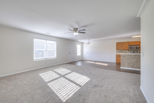 unfurnished living room with ceiling fan with notable chandelier, dark carpet, and crown molding