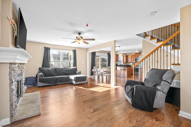 living room featuring light hardwood / wood-style flooring, ceiling fan, and a stone fireplace