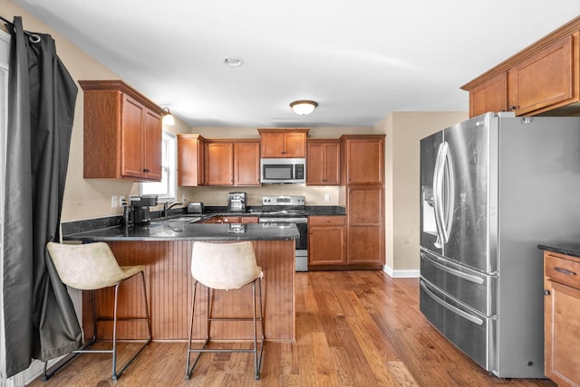 kitchen with sink, hardwood / wood-style flooring, appliances with stainless steel finishes, kitchen peninsula, and a breakfast bar area