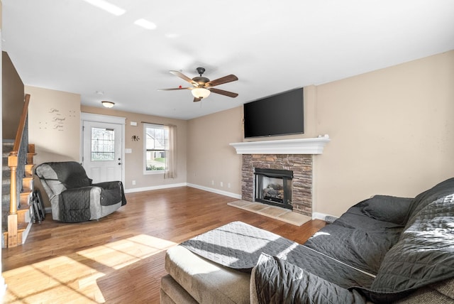 living room with ceiling fan, a stone fireplace, and wood-type flooring