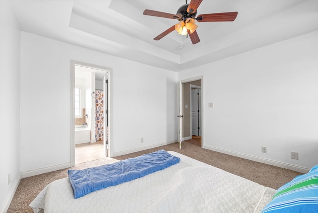 carpeted bedroom with a raised ceiling, ensuite bathroom, and ceiling fan