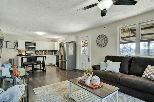 living room with a textured ceiling, dark wood-type flooring, ceiling fan, and a healthy amount of sunlight