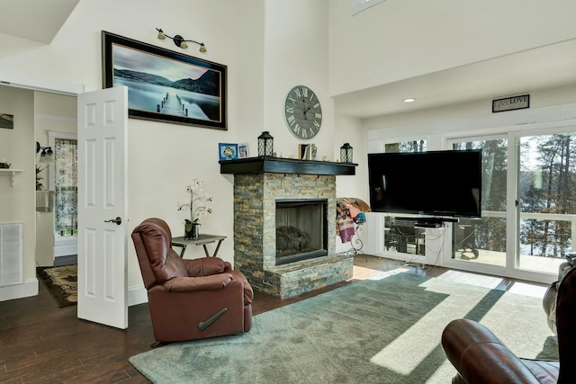 living room featuring a stone fireplace, dark wood-type flooring, and a high ceiling