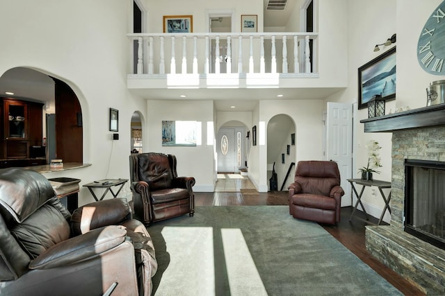 living room featuring a towering ceiling, dark hardwood / wood-style floors, and a stone fireplace